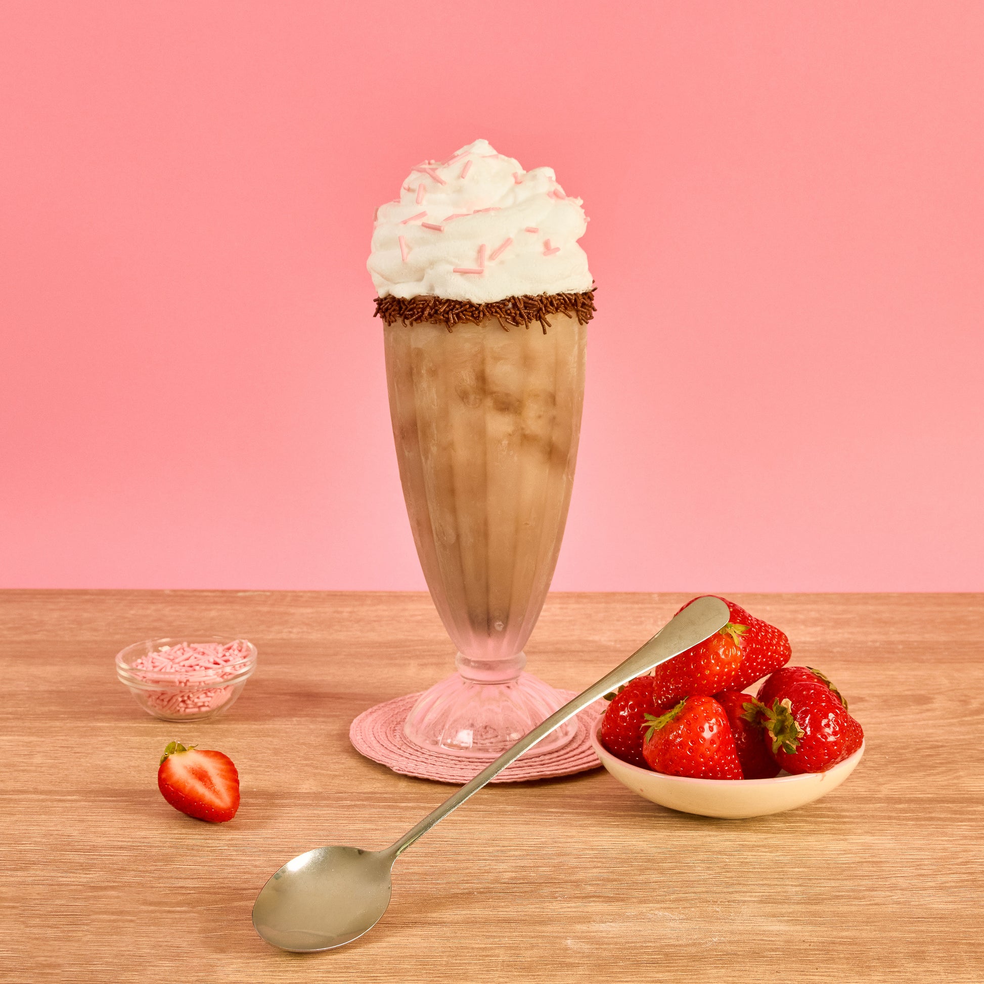 Long handled silver dessert spoon styled with chocolate milkshake whipped cream fresh strawberries and sprinkles for sundaes ice cream milkshakes and sweet treats