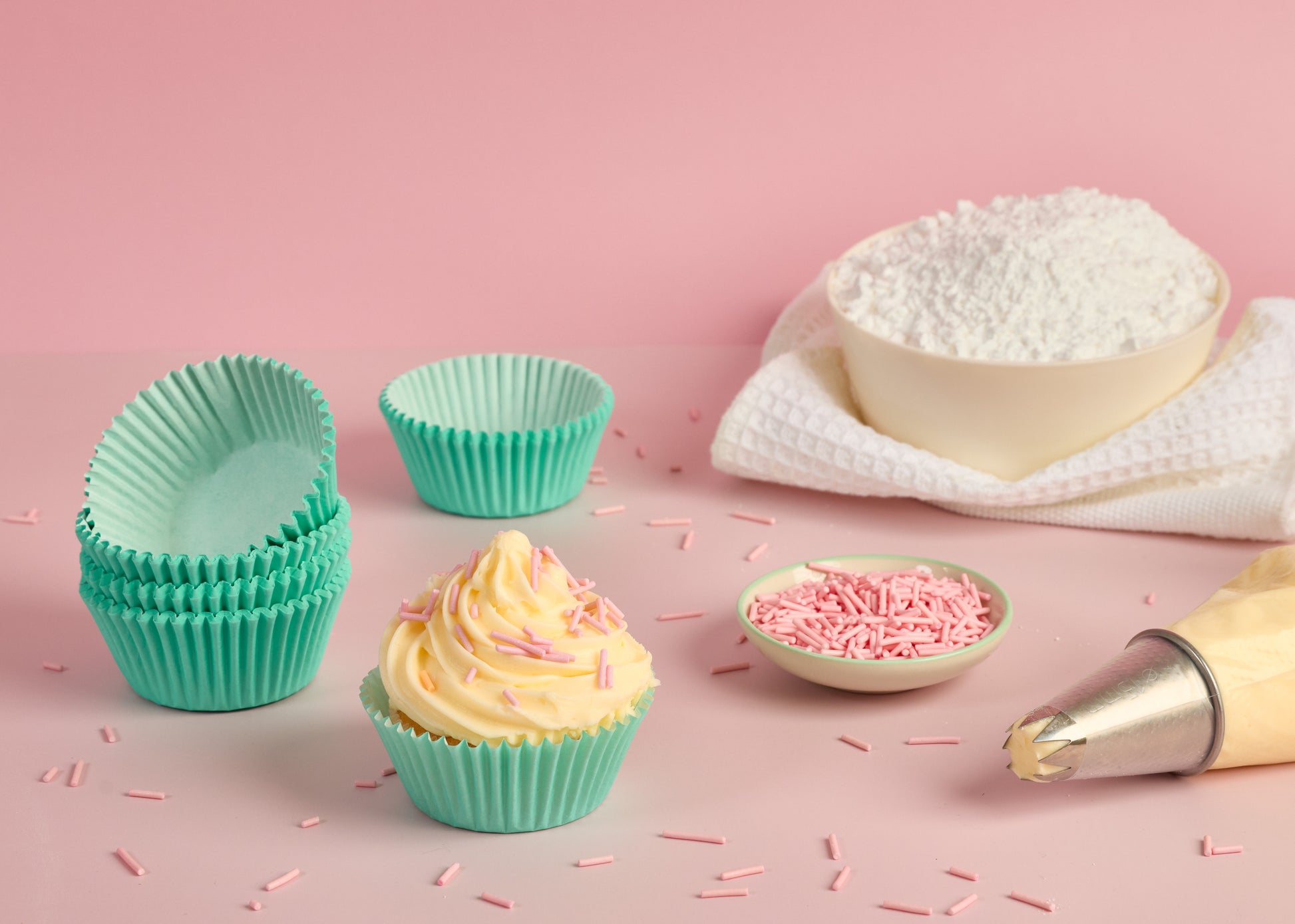 Mint green cupcake cases styled with a decorated cupcake piping bag cake sprinkles and baking ingredients for cupcake decorating and home baking