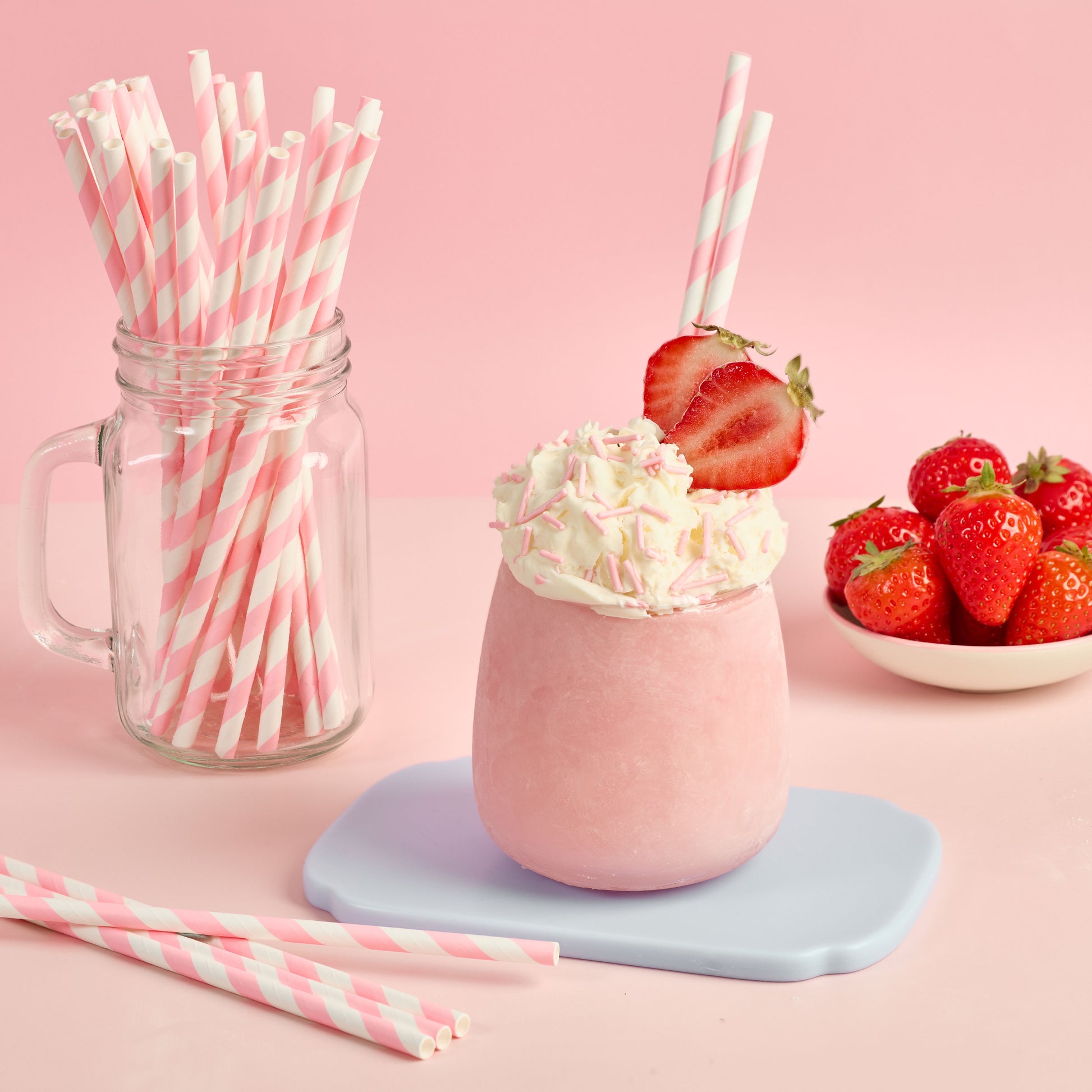 Pink milkshake with whipped cream and strawberries pink straws and a jar of additional straws on a pink background, for smoothies dessert drinks and party celebrations 
