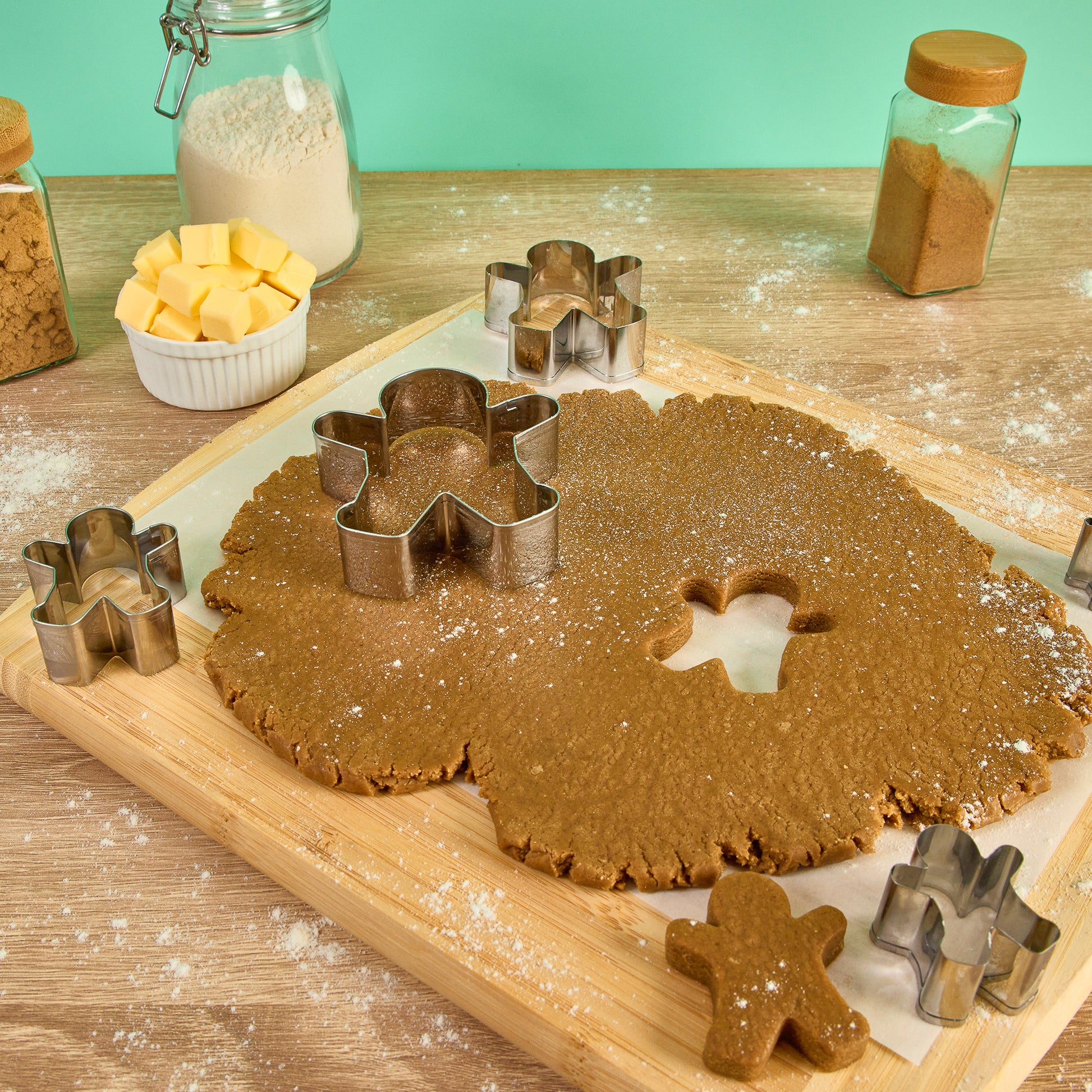 Metal gingerbread cookie set cutting gingerbread dough on a wooden board with flour,butter and baking ingredients